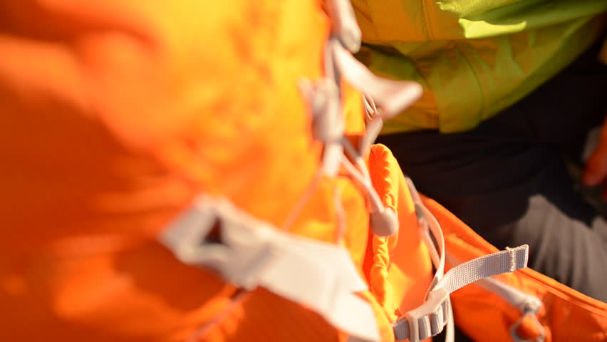 Close up as a hiker packs and prepares his orange backpack for a winter hike in the snow during the day