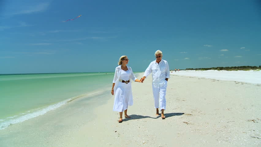 Attractive senior carefree couple walking along the beach barefoot enjoying a fun lifestyle 
