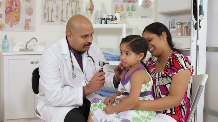 An Indian pediatrician or family doctor uses an otoscope to examine the ears of a little girl who is being accompanied by her mother.