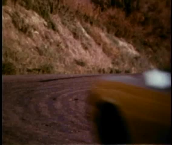 Woman driving 1970s car speeding down coast at sunset