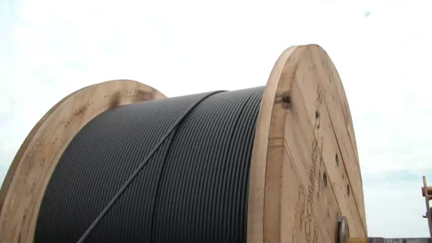 Clip of fiber optic cable being unreeled past workers and into actual pvc and hole underground.