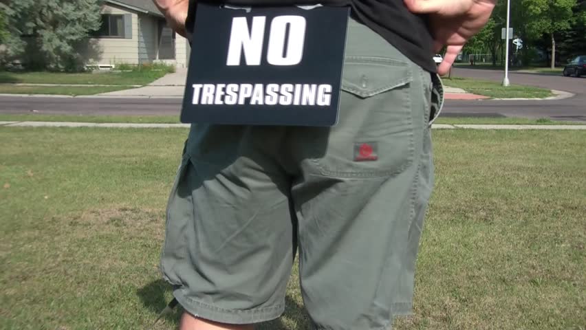 Man walks in yard with no trespassing sign attached to his butt, in sun.