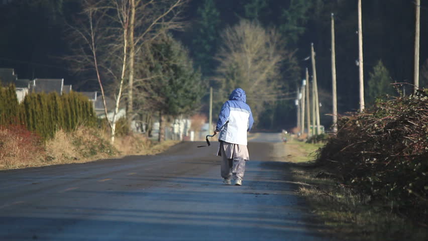 An old woman walks alone on a desolate, rural road