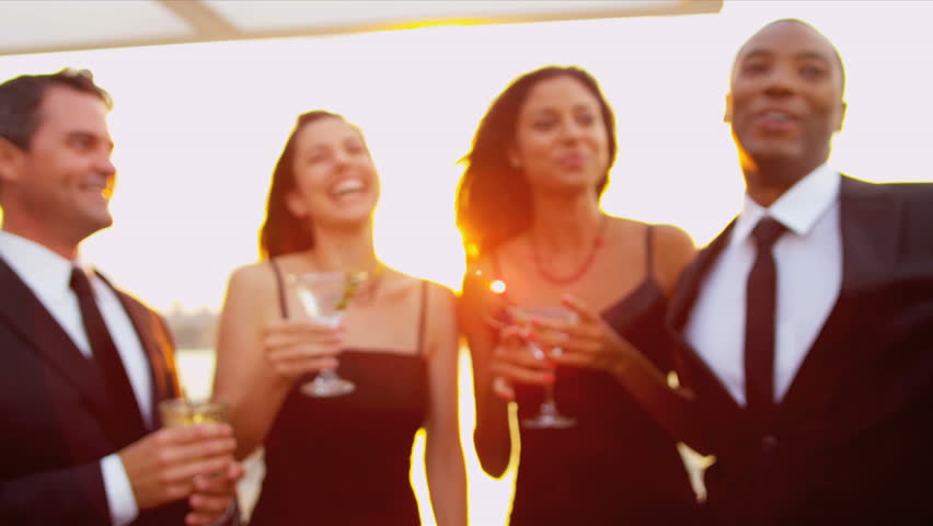 Smiling multi ethnic couples toasting at city cocktail party dressed in black sun lens flare shot on RED EPIC