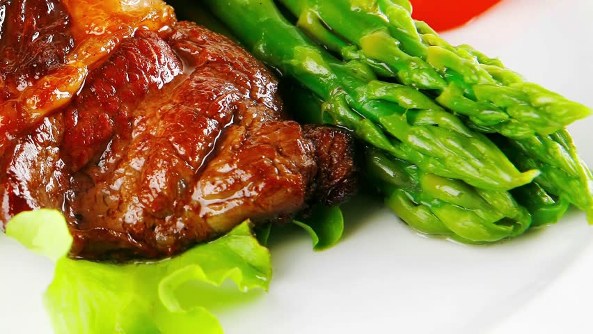 roasted beef meat served with asparagus on plate slow motion  hidef