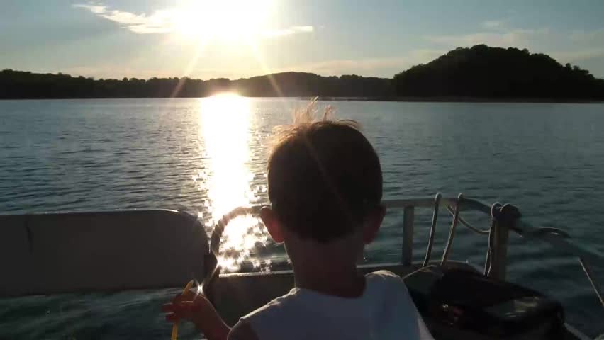 Little boy rides in the front of a pontoon boat, eating candy, and watching Minnesota scenery go by.