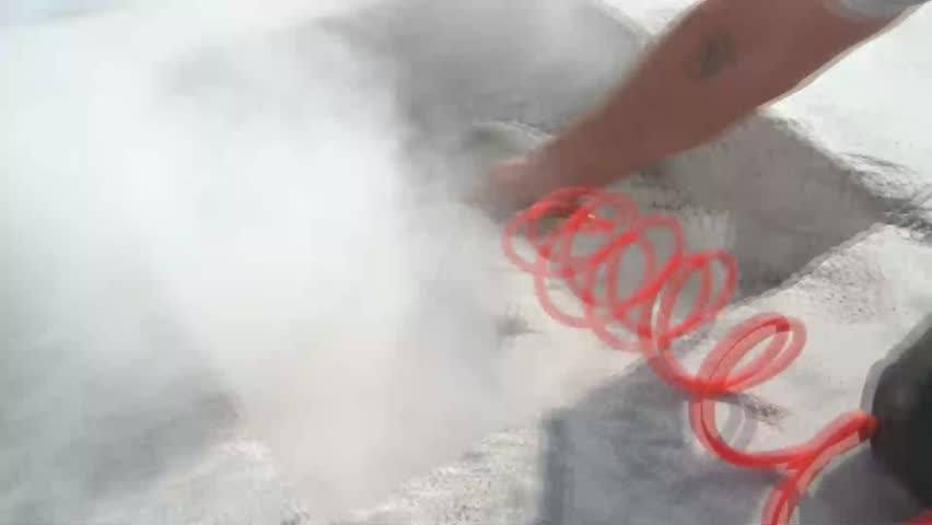 Worker blows dust with an air hose from a newly cut and drilled cement hole on sunny construction site.