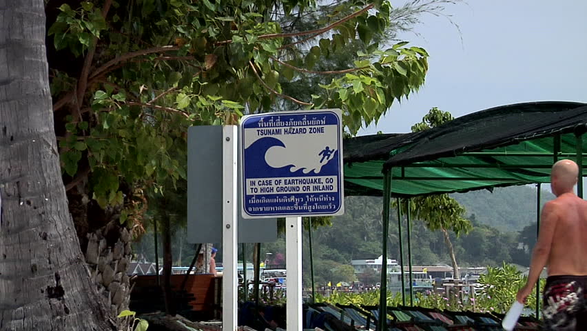 PHI PHI ISLAND, THAILAND - CIRCA FEBRUARY 2009: A Tourist passes a Tsunami Warning Sign