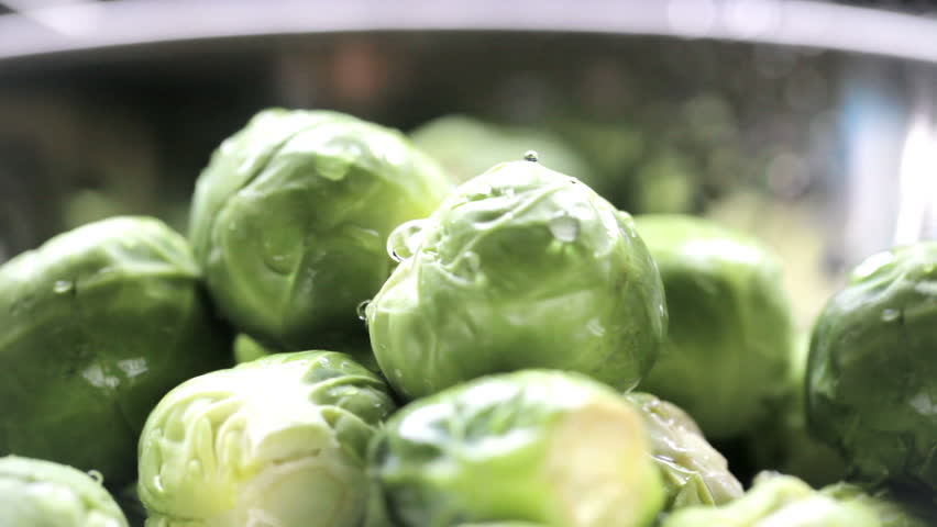 Close up of brussels sprouts being rinsed in colander .