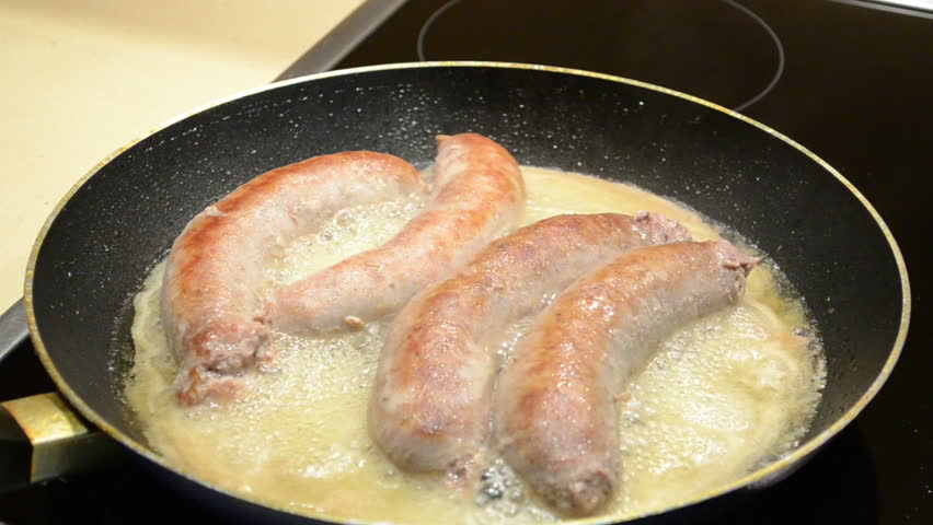 fresh meat sausages baking in pan. hand turns toasting meal.