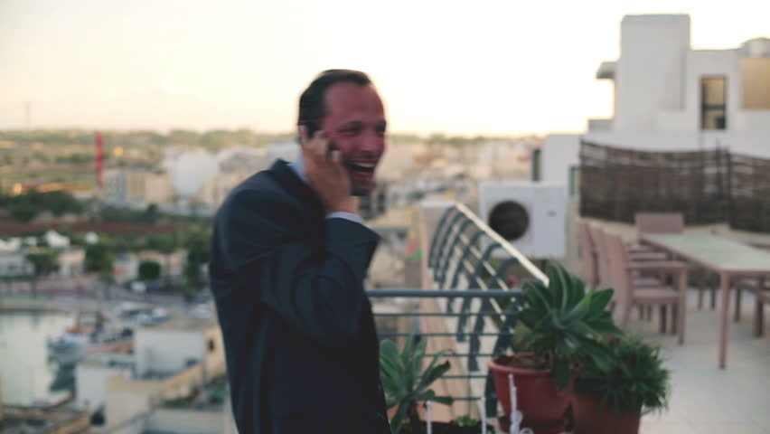 Businessman hearing great news on cellphone standing on the terrace, crane shot
