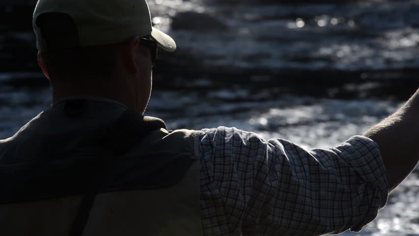 A man in waterproof overalls stands in a river and casts his lure with his rod while he spends his day fly fishing.