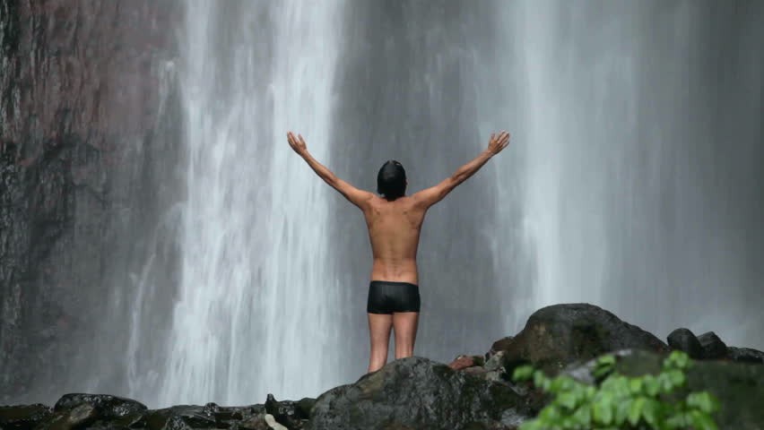 Man standing with arms up under waterfall in Bali, Indonesia
