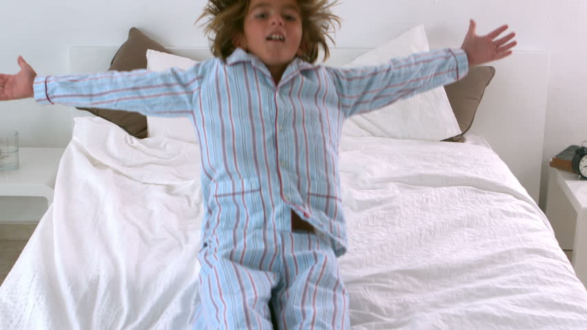 Little boy in pajamas jumping back onto bed in slow motion