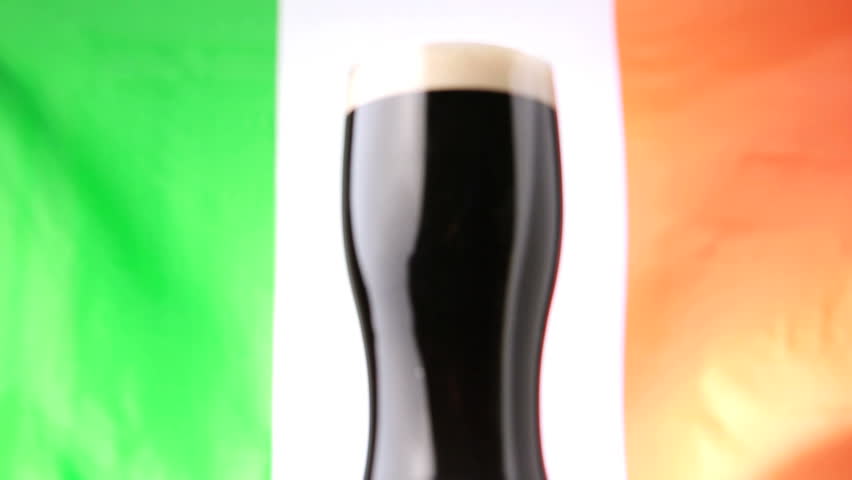 Pint of stout against irish flag blowing in the wind