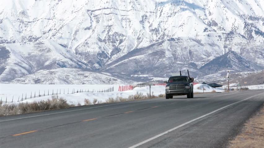Truck winter mountain rural road farms country. Winter rural mountain valley road with traffic pickup truck. Majestic snow covered mountain towers as a background. Farm and ranch land.