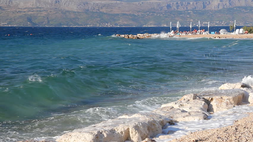 Waves splashing the beach, people sunbathe and enjoy on vacation, island Brac in Croatia
