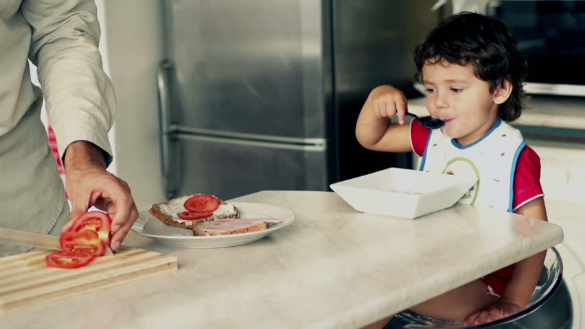 Little boy eating cornflakes with milk, father preparing sandwich, slow motion shot at 120fps

