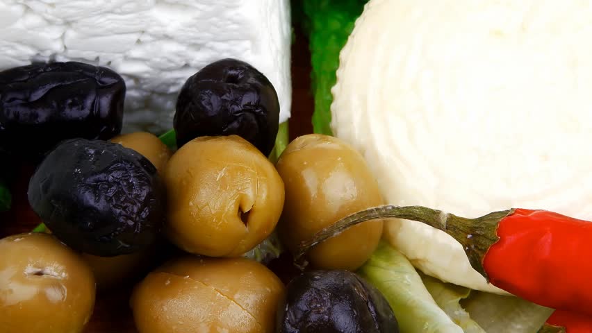 dairy food : feta white cheese cubes and round served on wooden cut plate with green leaves and olive oil isolated over white background