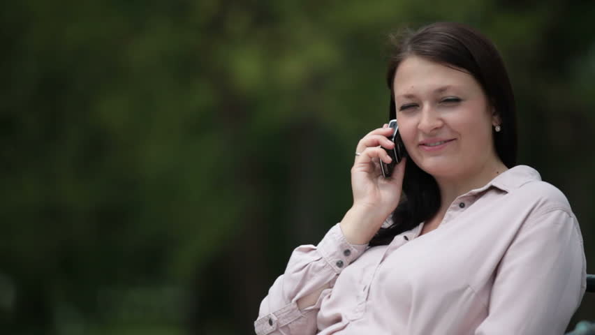 Smiling pregnant woman on the phone in city park