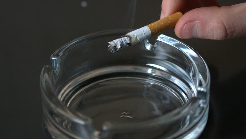 Hand tipping ash into empty ashtray in slow motion