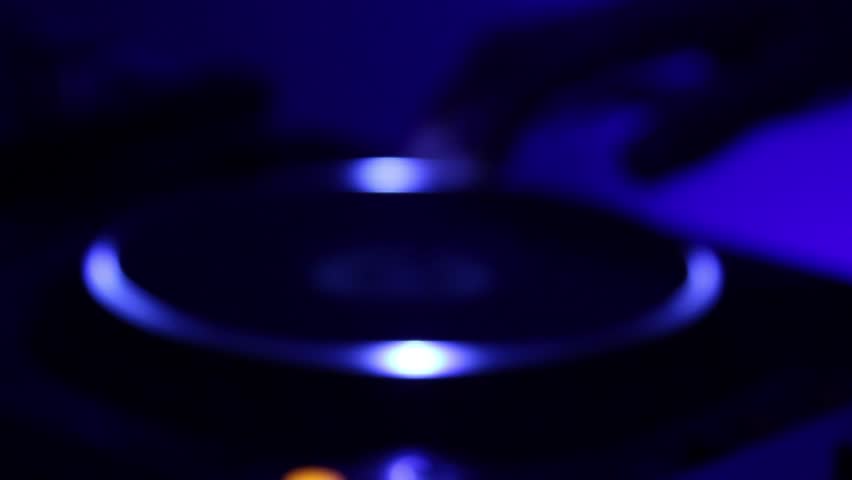 DJ's hand scratches the turntable in dark night club.