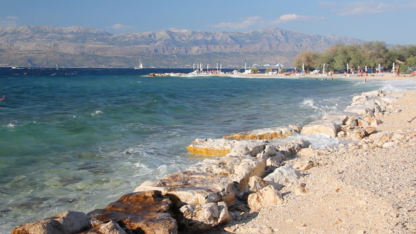 Waves splashing the beach, people sunbathe and enjoy on vacation, island Brac in Croatia