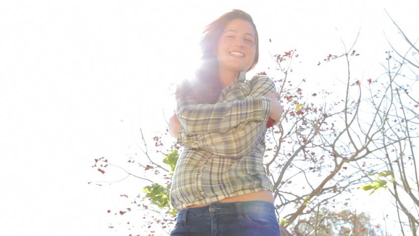 Attractive joyful young woman dancing and turning around on a sunny day against the sky and with the sun shining behind her and filtering through her body and face.