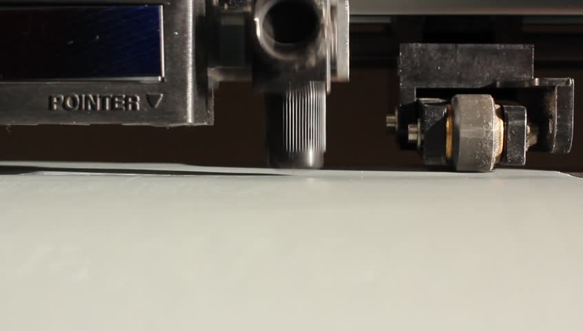 Cutting plotters use knives to cut the letters on gray vinyl film. Close-up view from below