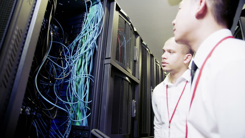 Group of  IT engineers of mixed ethnicity carry out an inspection and maintenance procedure on servers and computers in a data center.