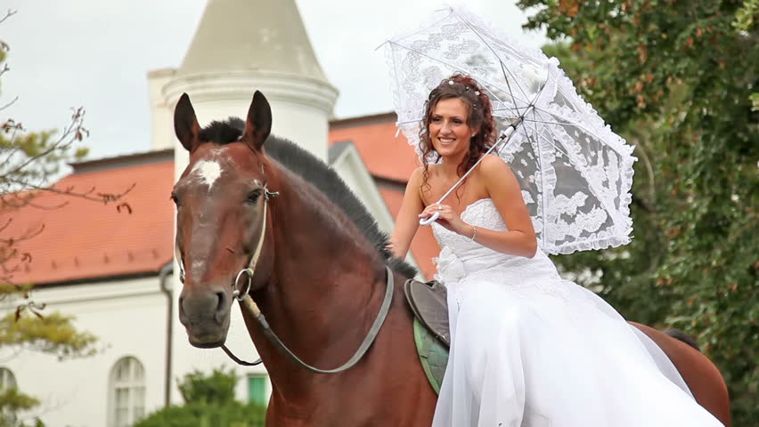 Happy bride riding a beautiful brown horse in the garden