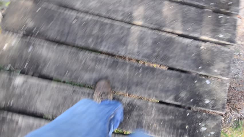 Man walks on a wooden bridge over small stream in the wilderness. 