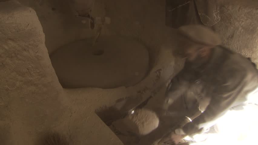 North-east of Fayzabad, Afghanistan - November 12, 2010: Man working in a water powered mill. Scooping flour into a sack while millstone is rotating.