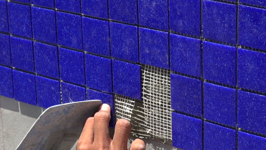 pool tile installation, laborer's hands installing blue swimming pool tile with trowel, tripod