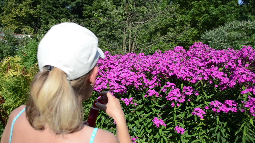 young woman with bra and white cap on head blow soap bubbles on background of red flowers in garden.