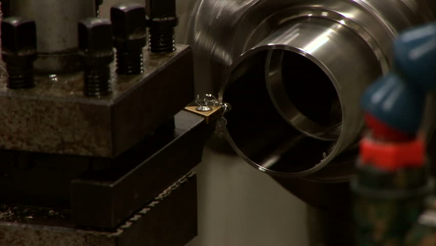 A close up of a stainless steel tube turning on a metal lathe.