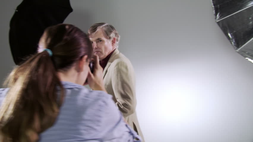 Female photographer takes pictures of male actor/model. Deliberately edgy, hand-held camera in studio with focus on subject.
