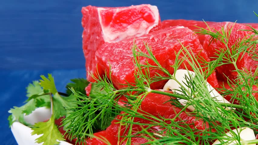 slices of raw fresh beef meat fillet in a white bowls with dill and green peppers serving over blue wooden table