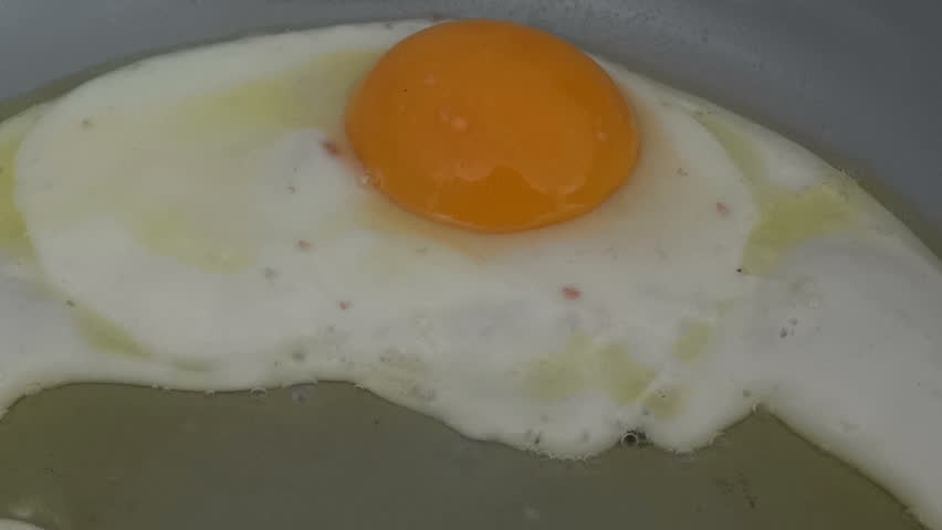 Egg frying in oil in a ceramic frying pan.
