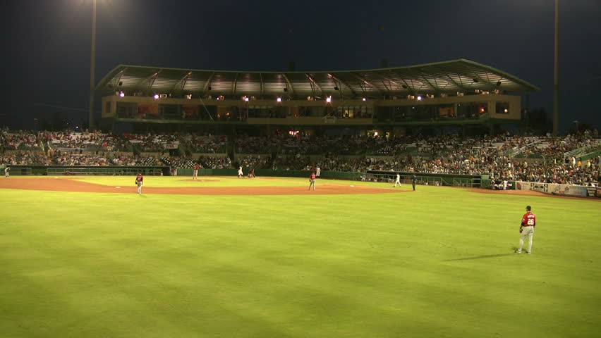 Video of a baseball stadium at night from the outfield fence. Night time with glowing playing lights. Stadium full of spectators. Player on the field. Don Despain of Rekindle Photo