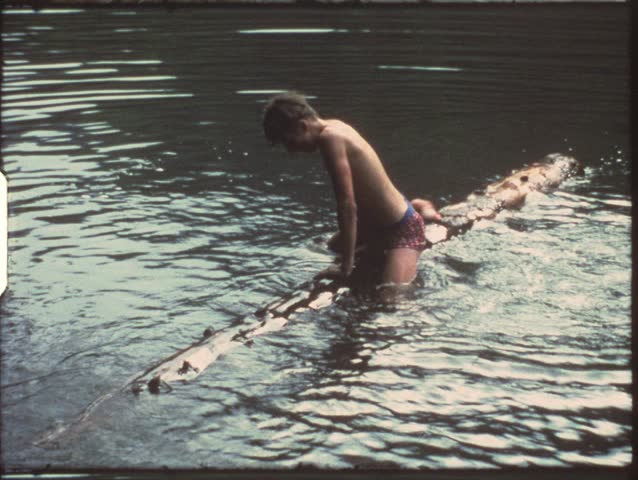 Vintage 8mm film: Boy riding on tree log in lake