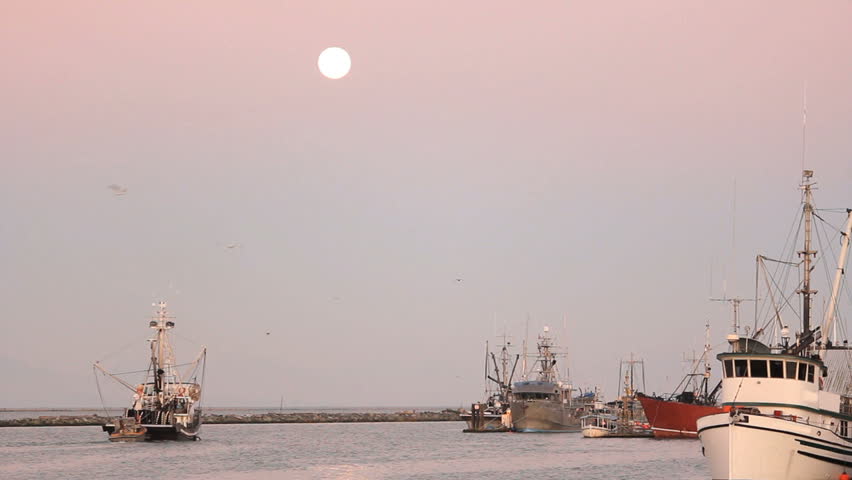 Full Moon, Steveston Harbor, Fishboat Departs. A fish boat departs Steveston Harbor on the Fraser River in British Columbia, Canada at sunrise as a full moon is setting.