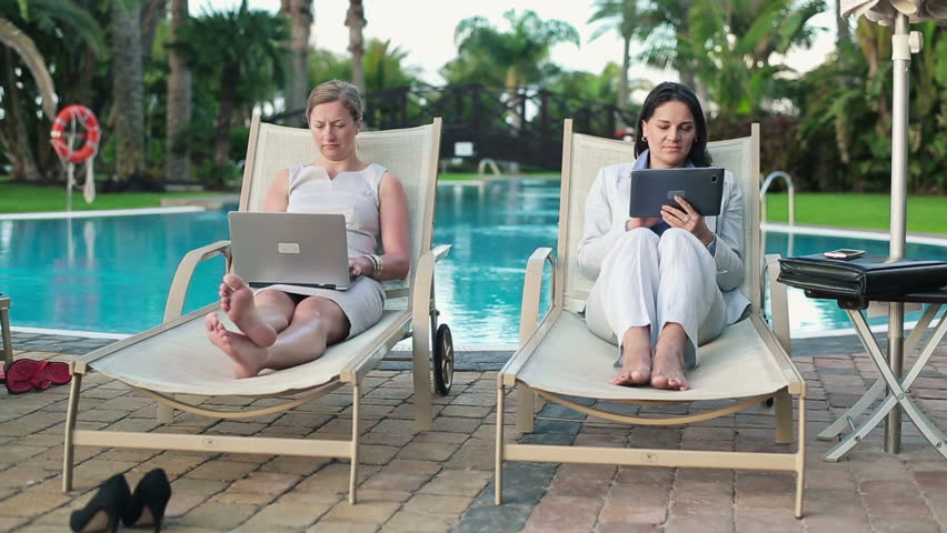 Businesswomen with laptop and tablet relaxing on sunbeds
