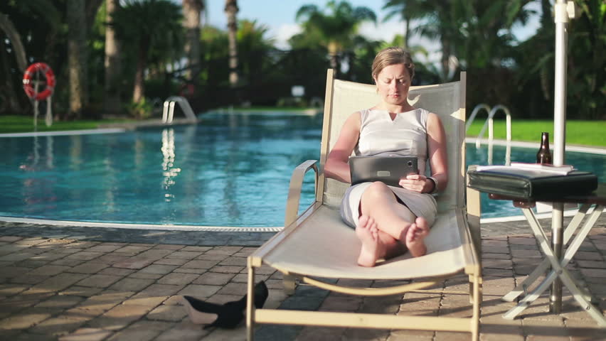 Businesswoman on sunbed using tablet computer by the pool
