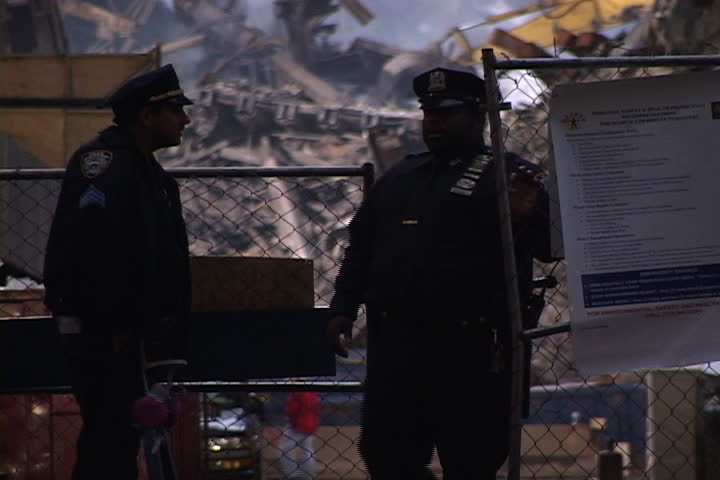 NEW YORK CITY - SEPTEMBER 28, 2001: Two police officers stand at gate in front of ground zero. Smoking rubble and construction vehicle in background.