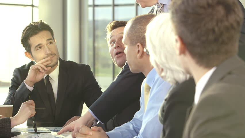 An attractive and happy business team of mixed ages and ethnicity are holding a meeting in a light, modern office building. They are brainstorming for ideas for their business development. 