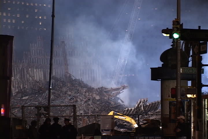 NEW YORK CITY - SEPTEMBER 28, 2001: Smoke rising from floodlit rubble at World Trade Center site. Emergency workers walk past.