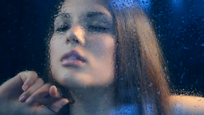 Beauty Woman Behind Wet Rain Window. Melancholy Woman. Beautiful Model Looking Through the Window with Rain Drops 