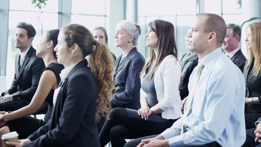 A multi ethnic group of business people of mixed ages are listening to a presentation at a business seminar and asking questions.
