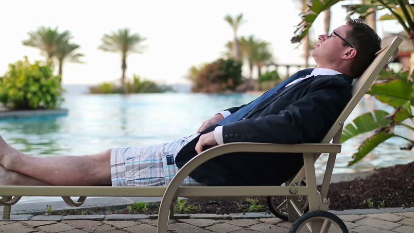 Happy businessman relaxing on sunbed by the swimming pool
